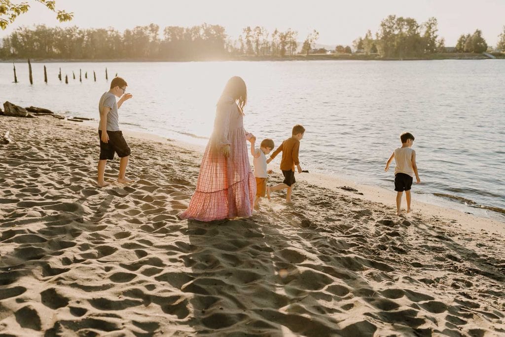 Mom in pink free people dress walkin on the sand with her three boys