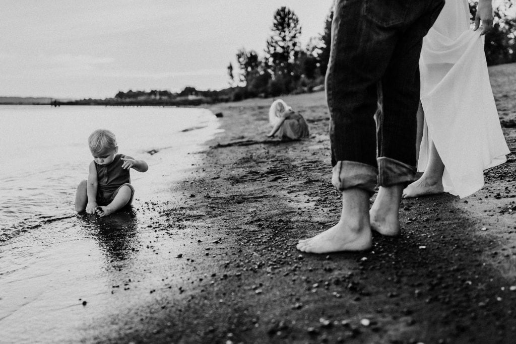 Black and white image of parents feet with kids playing on the water - Oregon coast family photographer