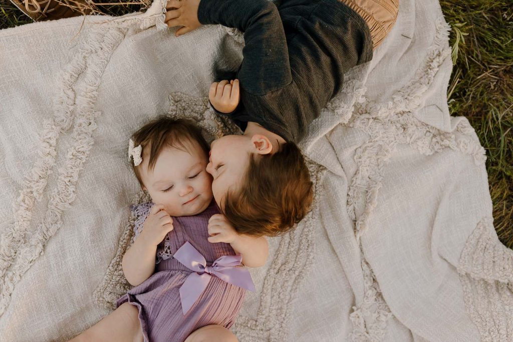 toddler boy kissing baby sister on blanket