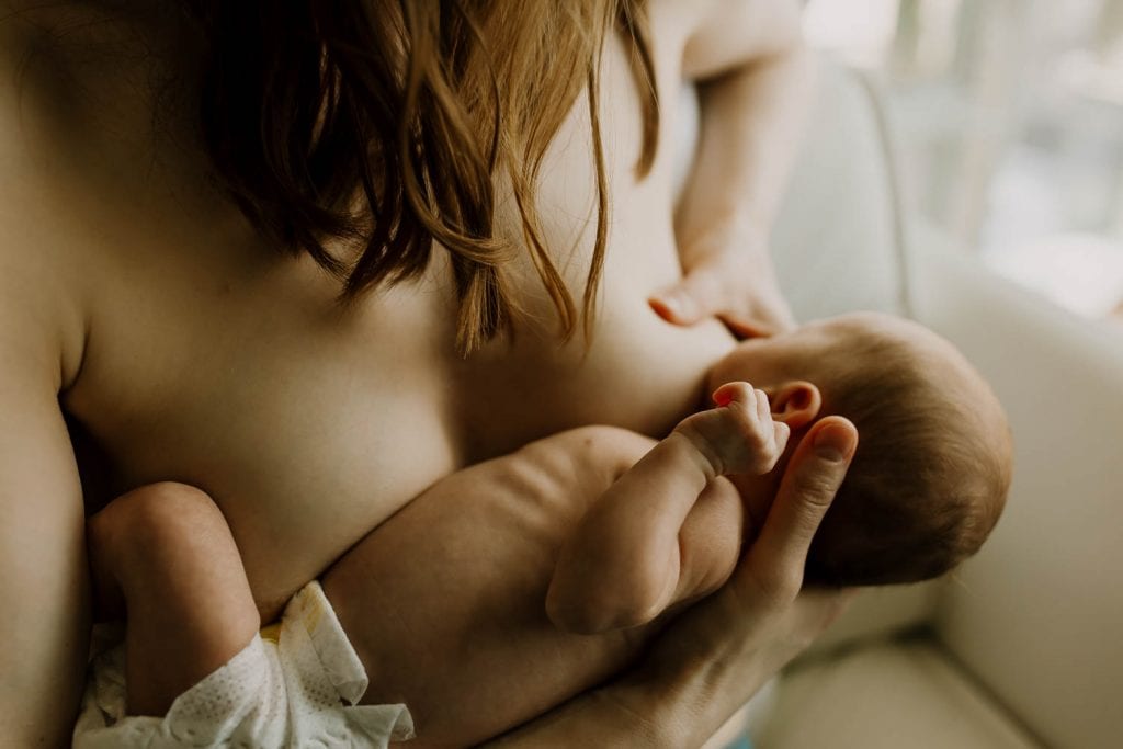 Mom nursing her newborn baby skin to skin with moody lighting - breastfeeding portland photographer