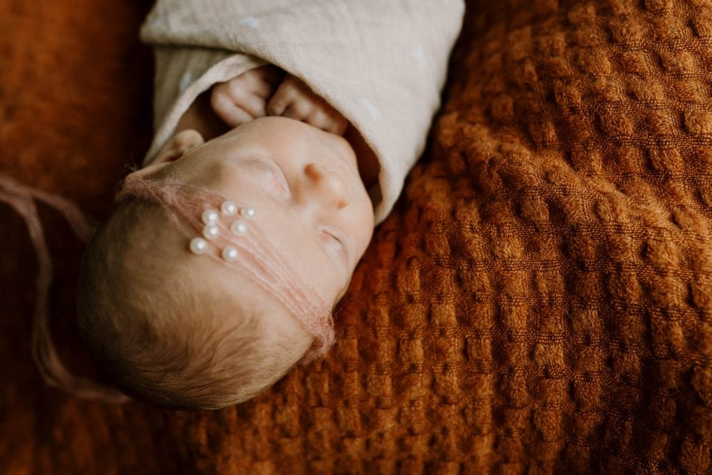 sleeping newborn baby girl on rust blanket wearing delicate headband