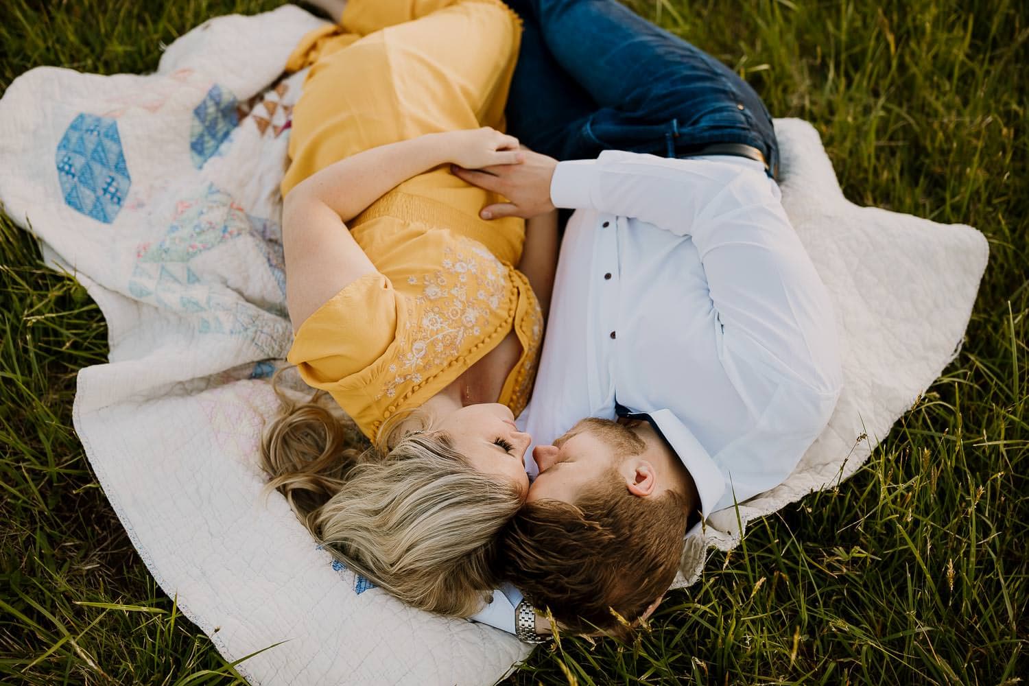 Pregnant couple laying on blanket in grass