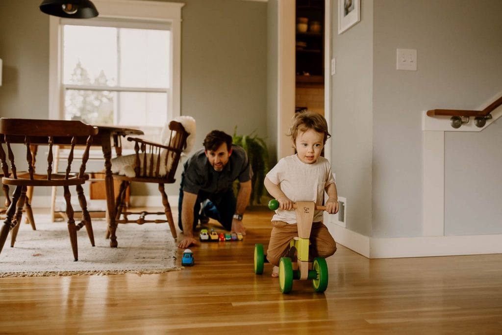 Dad chasing toddler on wheels during in-home documentary session