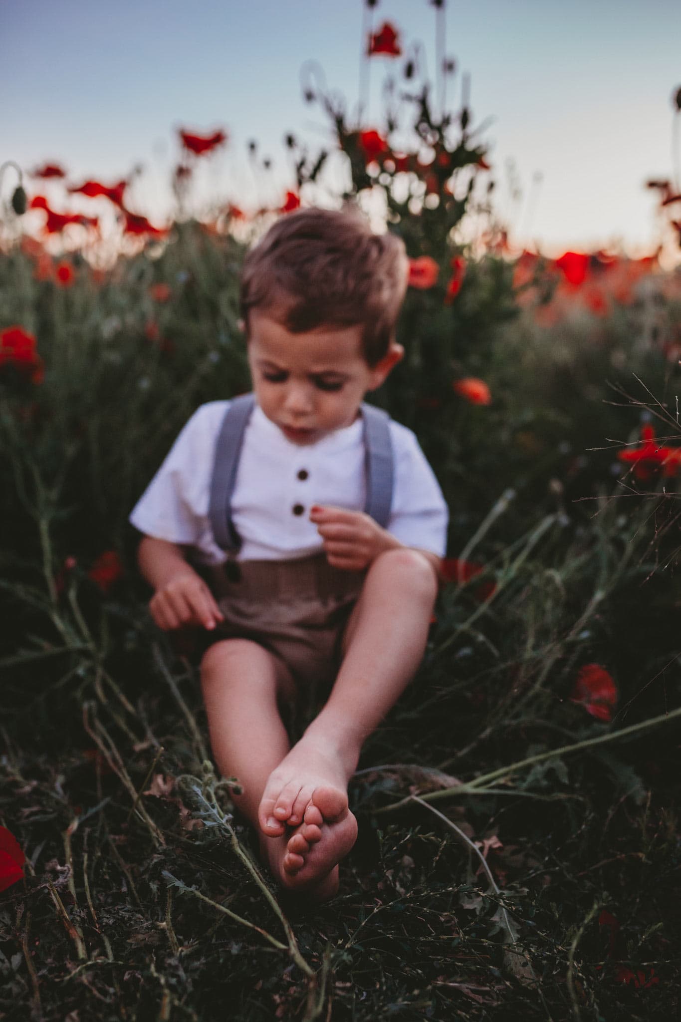 Toddler boy sitting in flowers with the focus on his feet