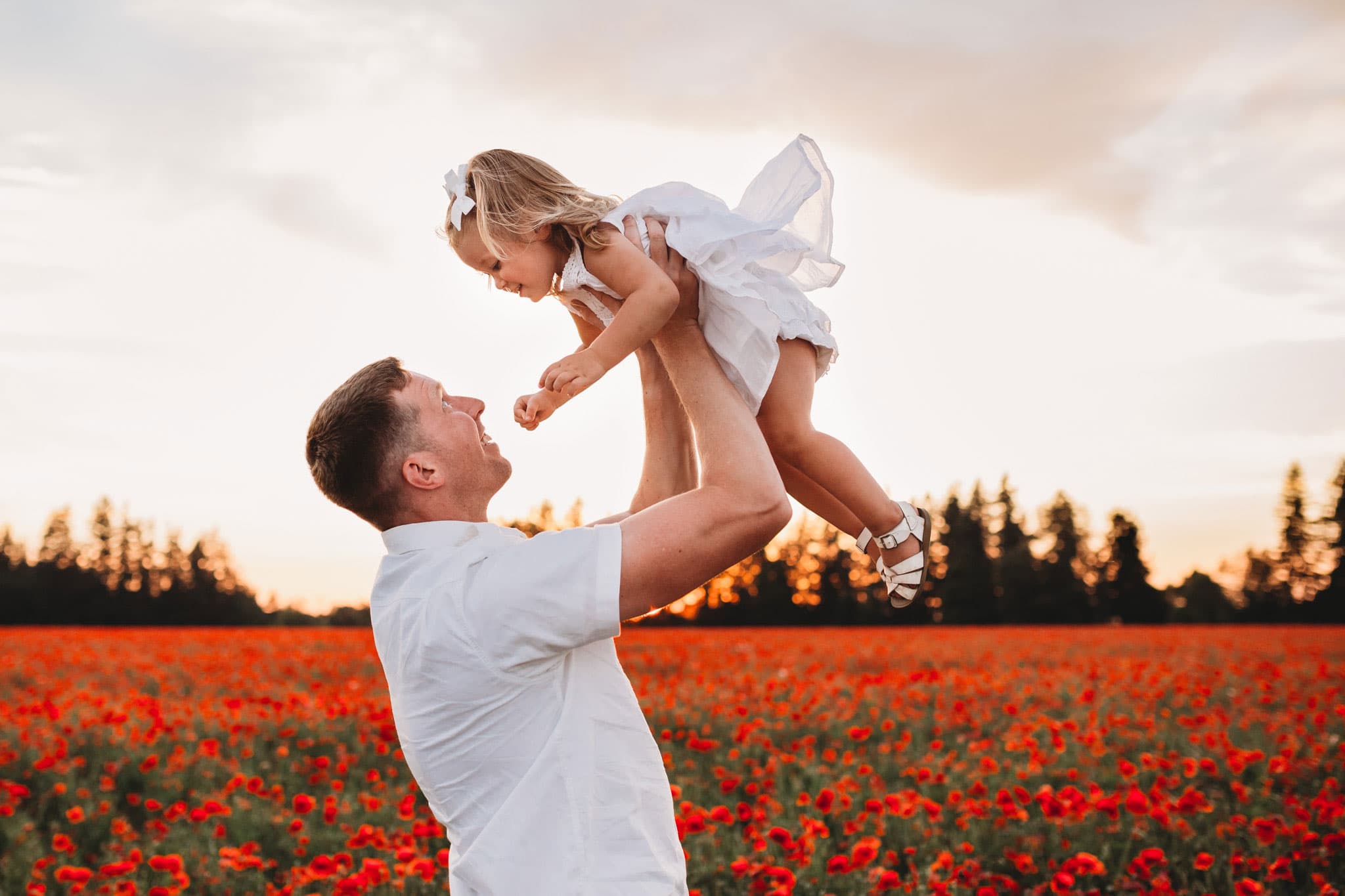 Dad holding toddler baby girl with poppy fields behind them