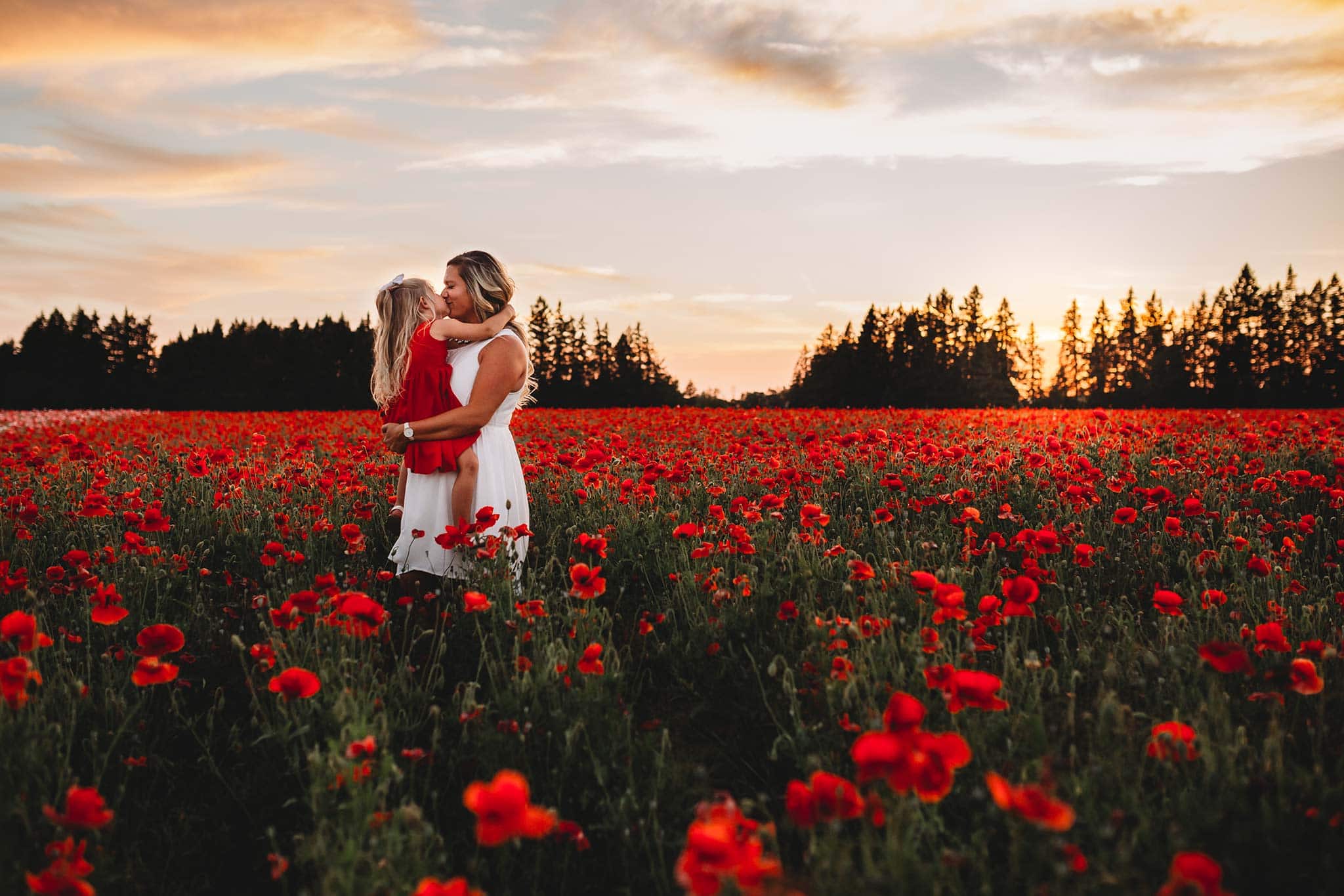 Daughter kissing mom while standing in Oregon fields of poppies