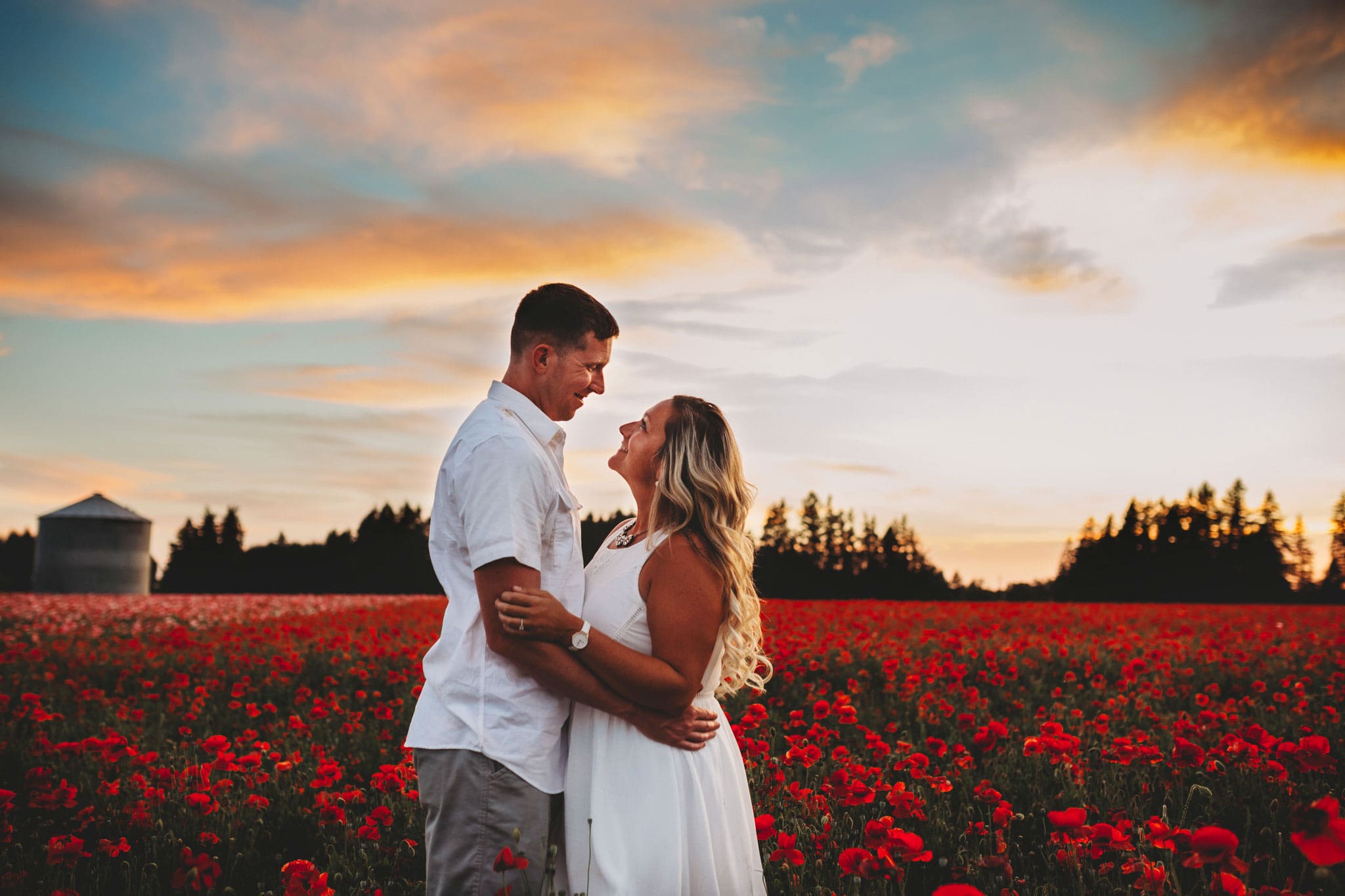 Parents looking at each other and hugging in Oregon red Poppy Fields with sunset behind them