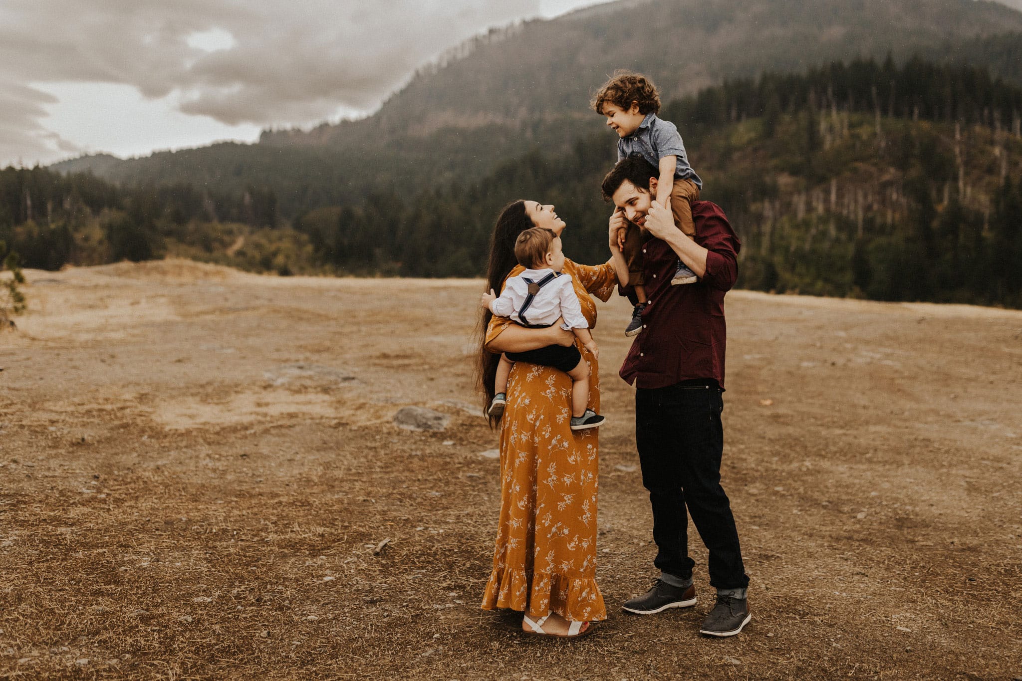 dad holding son on shoulders, mom holding abby boy, all standing close on a mountain while sprinkling. Fall family photos in Portland Oregon