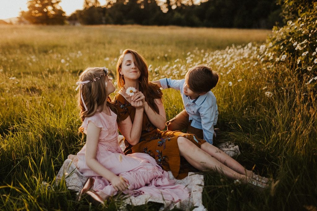 mom sitting in grass with kids, smelling flowers