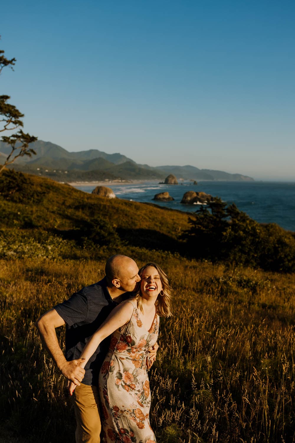 married couple laughing with cannon beach behind them