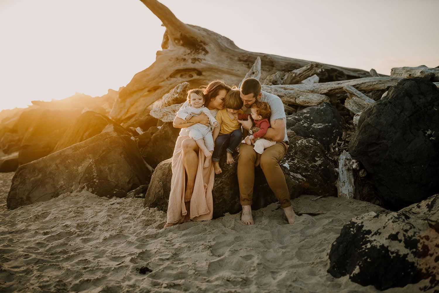 Family cuddling on driftwood and rocks on the oregon coast