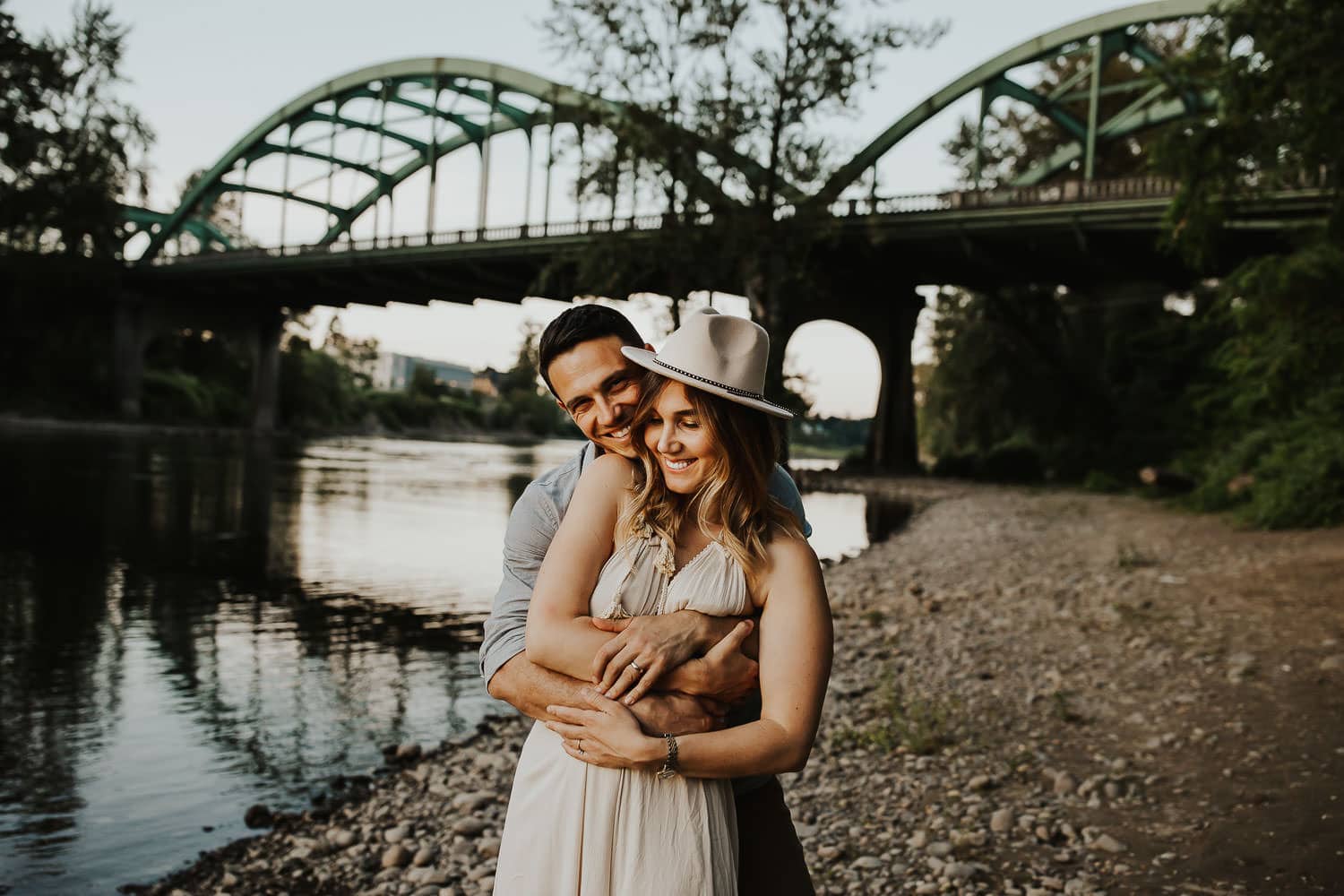 Couple smiling and cuddling together with bridge in background near Portland Oregon