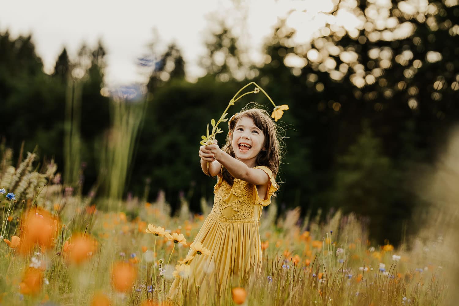 5 year old girl holding up a yellow flower and smiling at it