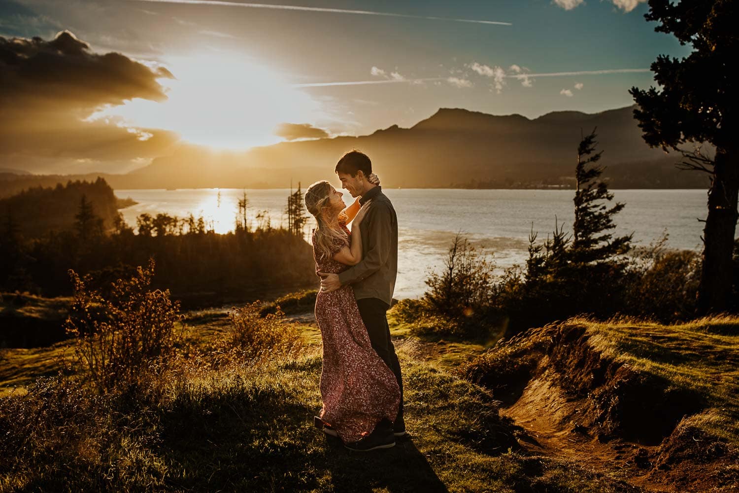 Couple looking into each others eyes holding each other with the sun setting behind them