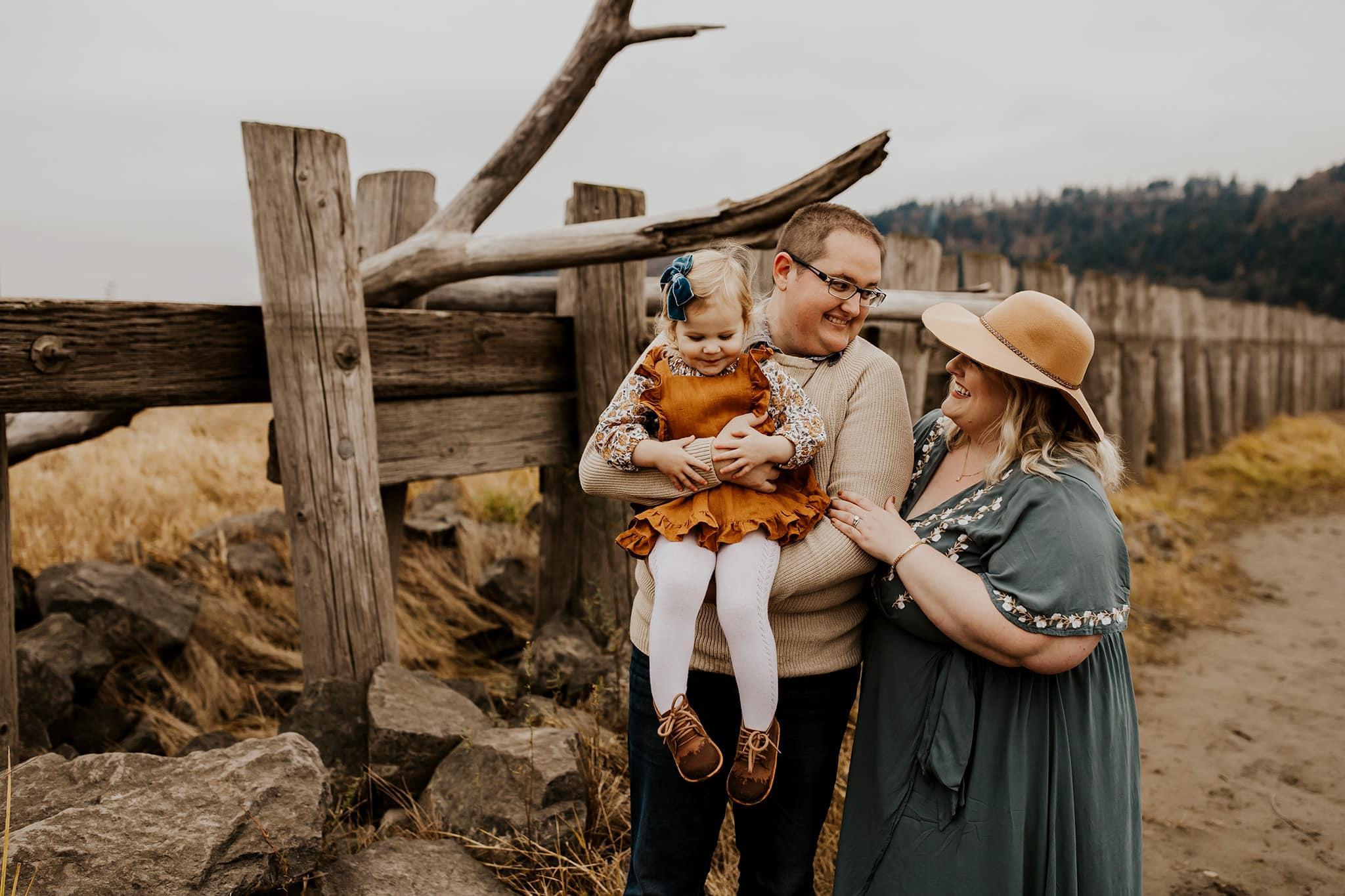 Family of three with wooden fence behind them on a cloudy day near Portland, oregon
