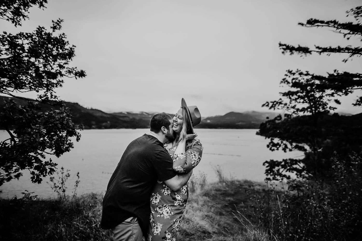 black and white image of a couple laughing together with river behind them