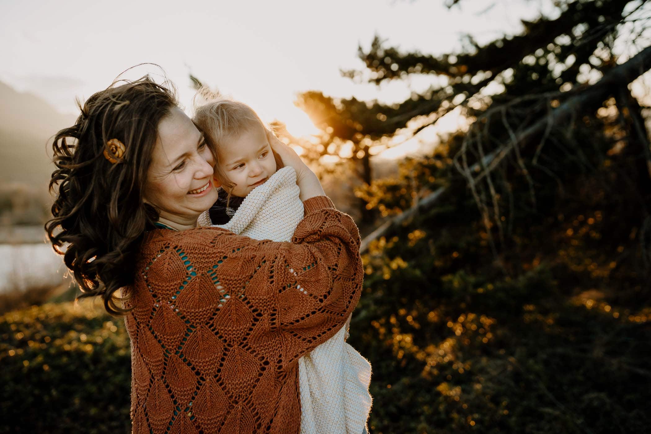 Mom in a brown cardigan holding toddler son with sunset behind - clubhouse app for family photographers
