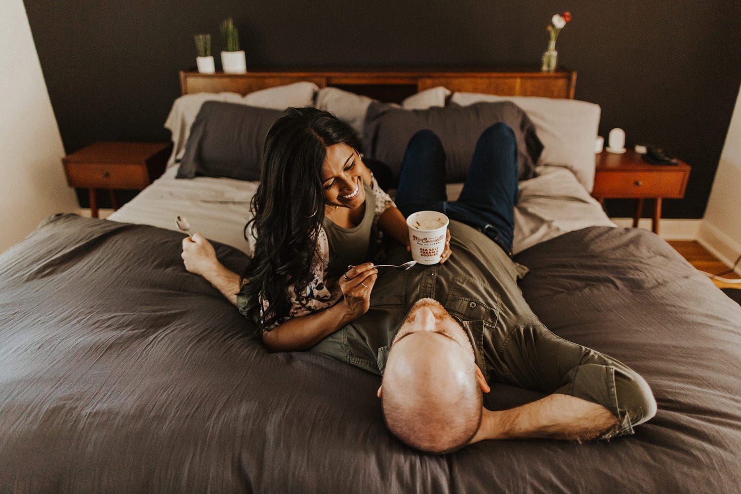 Portland couple laying in bed eating ice cream together and smiling - anniversary date night ideas
