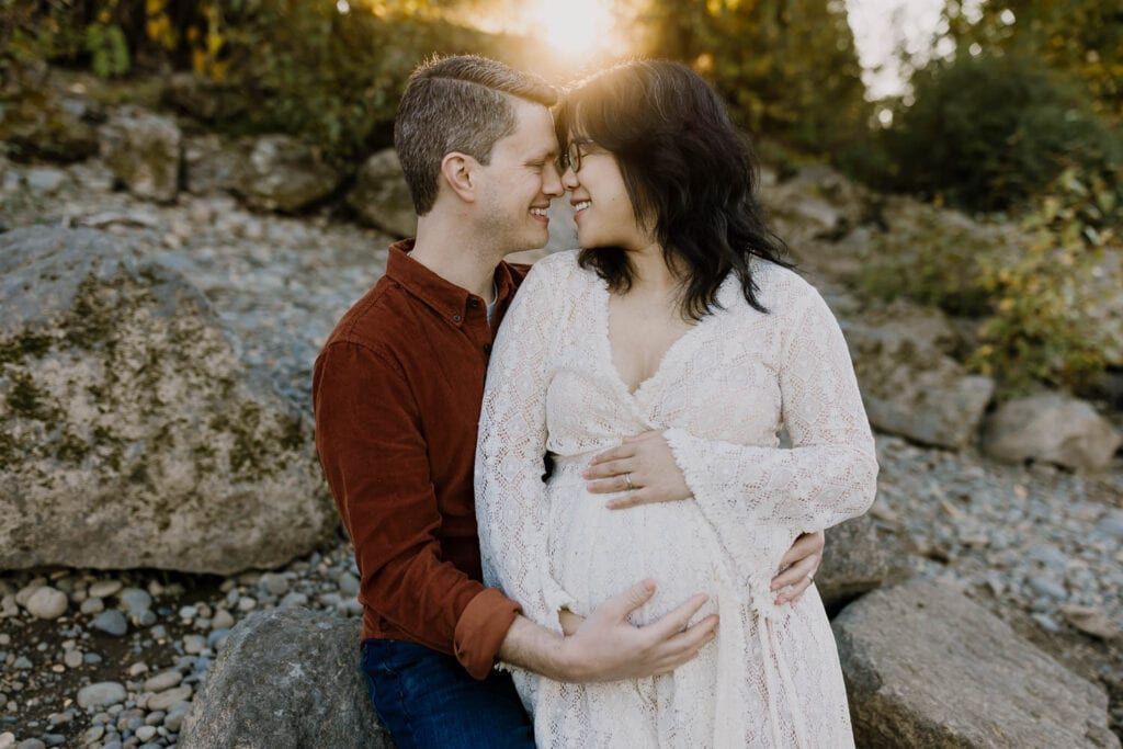 25 weeks pregnant woman in lace dress holding her belly while husband cuddles her