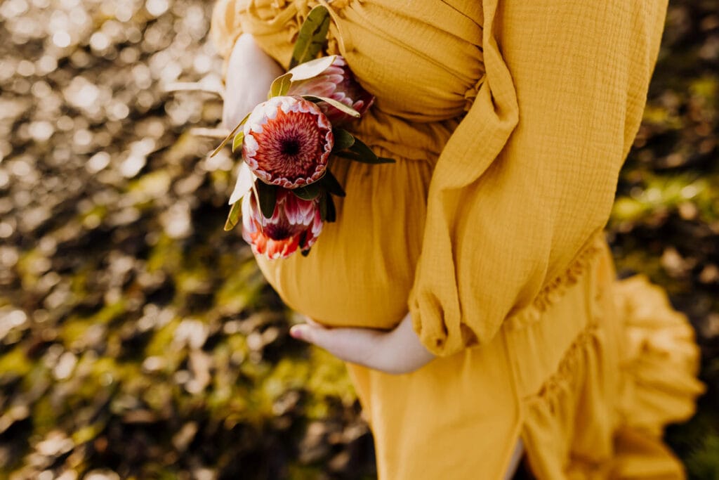 pregnant belly in a yellow dress holding flowers during maternity photos