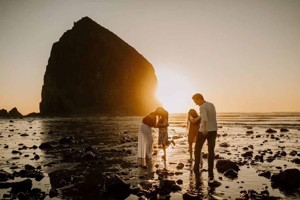 photo of a family playing on the beach with the golden sunset peeking past haystack rock