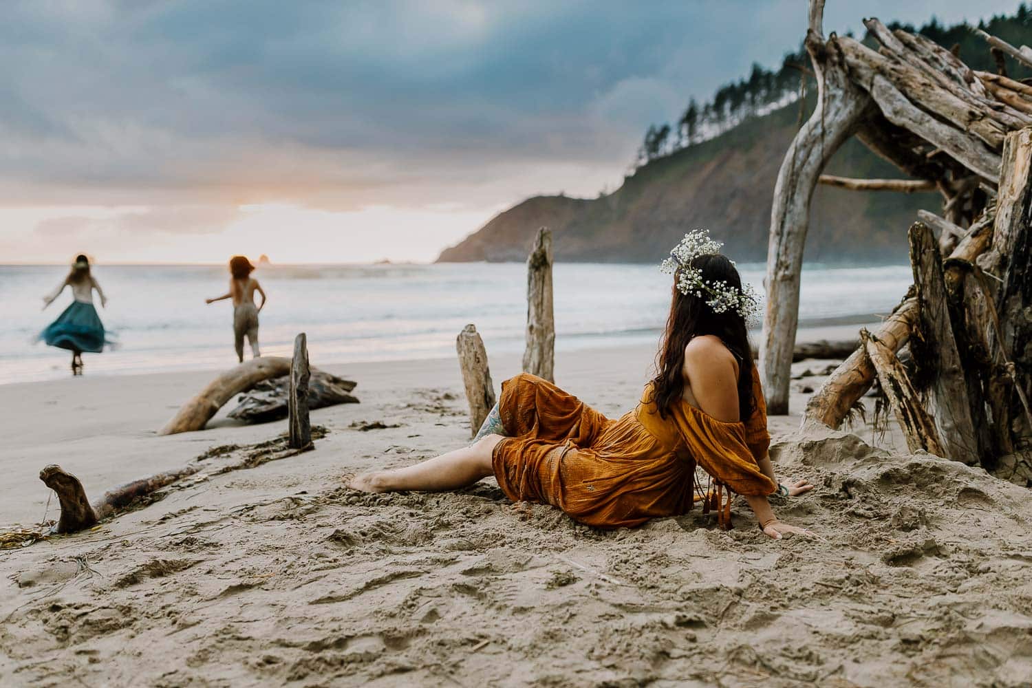Mom sitting on sand in free people dress staring at her kids running to the water - best oregon coast family photographers