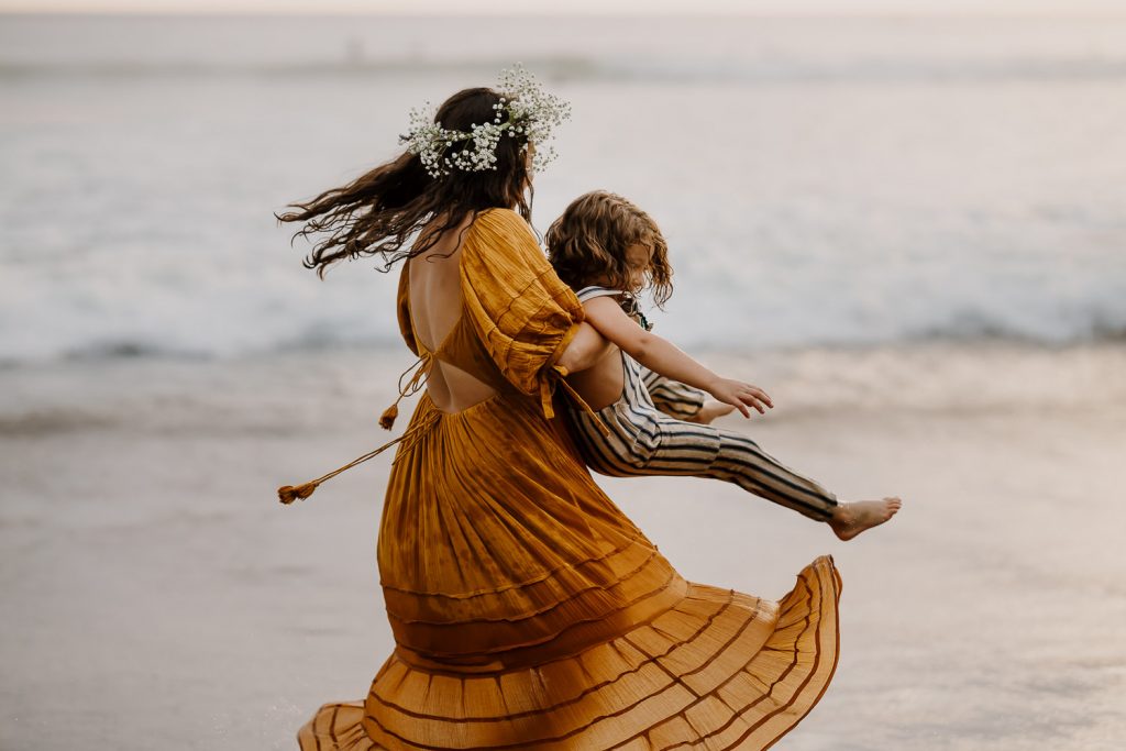 Mom in free people dress spinning with her son at the beach