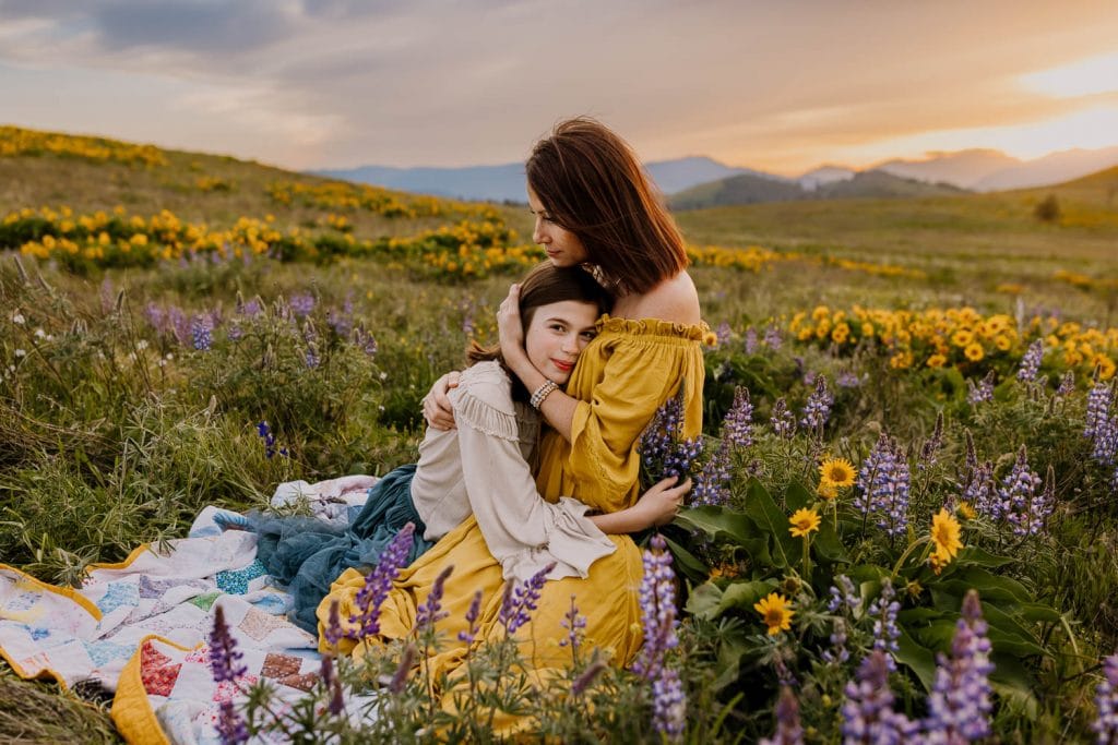 Mother hugging daughter on a blanket in the wildflowers