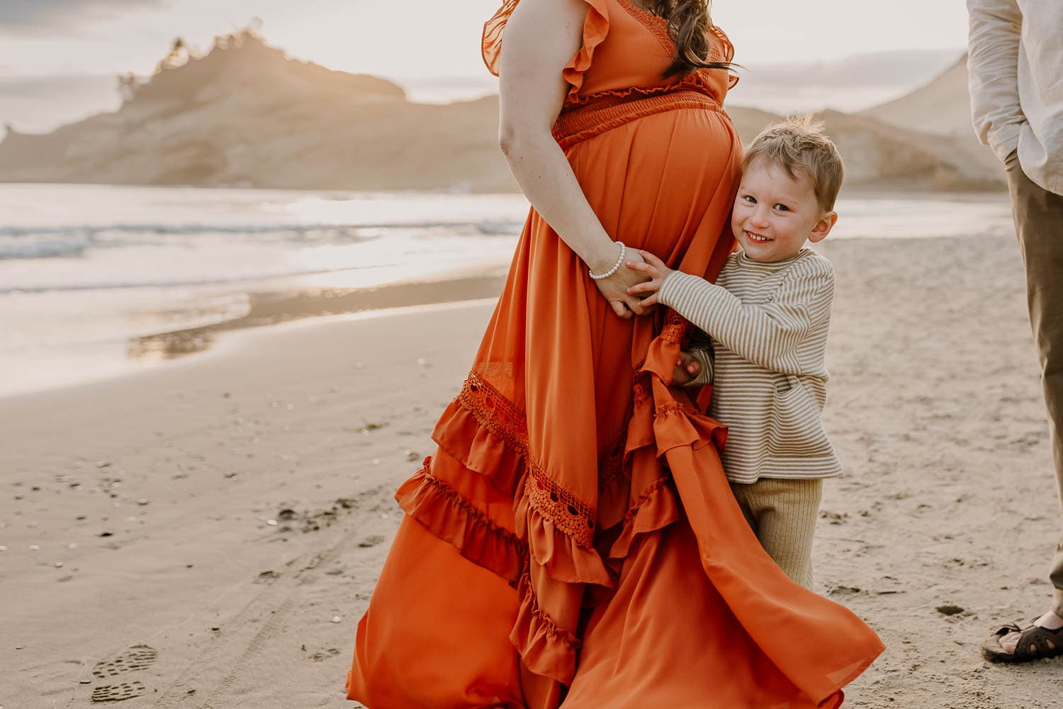 Little boy hugging onto his pregnant mom during family photos in cape kiwanda