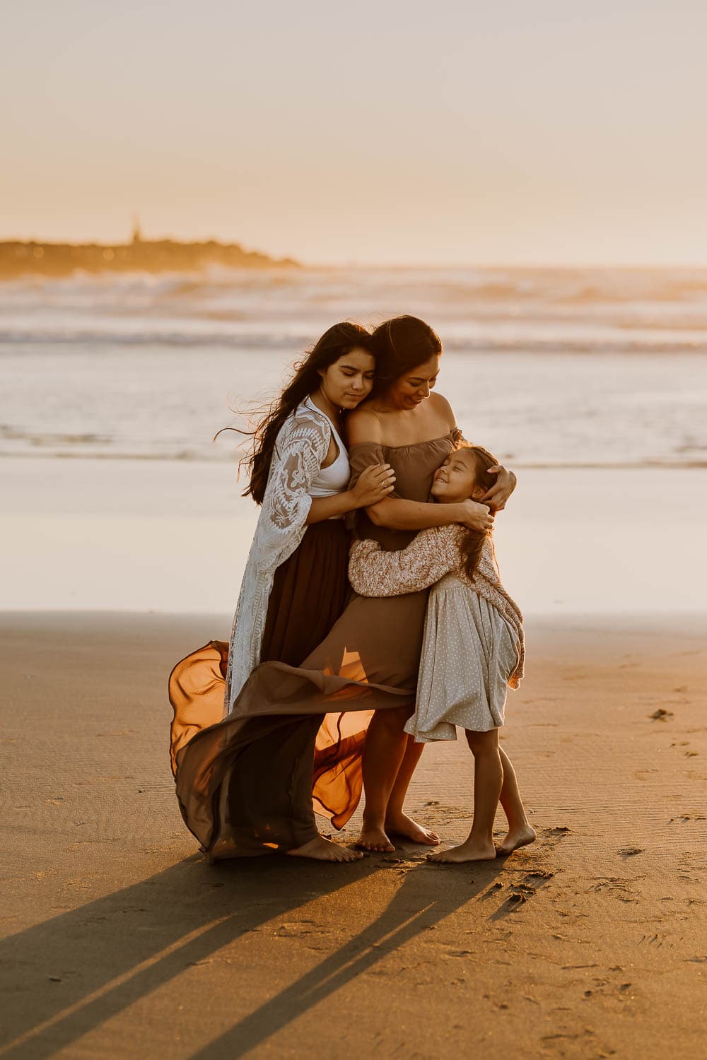 mom and two daughters hugging on the beach on rockaway oregon during family photos