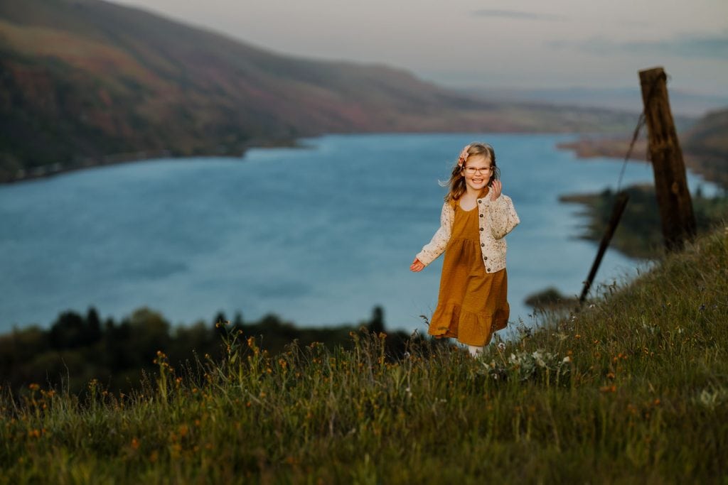 Smiling and happy little girl on a hill of flowers with the columbia river behind her near Portland