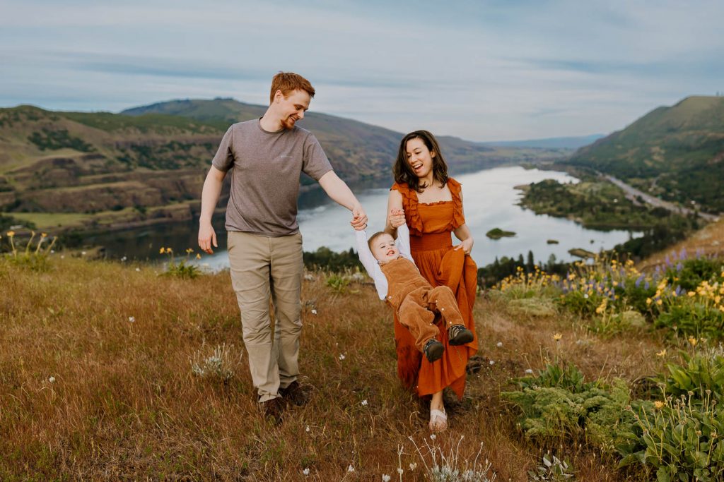 Family walking together and swinging toddler son with the columbia gorge behind them