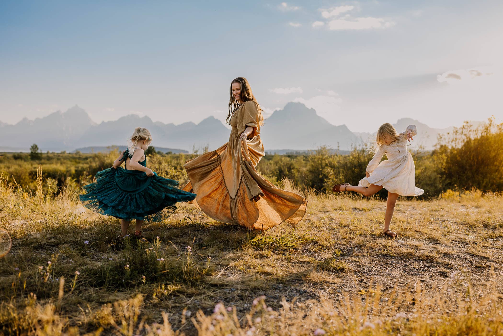 mom and two young daughters twirling their dresses in the grand tetons