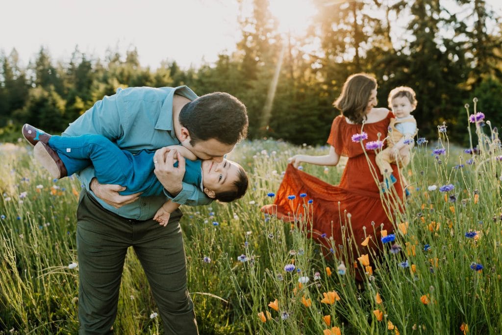 dad kissing little boy in blue romper, while mom spins with toddler