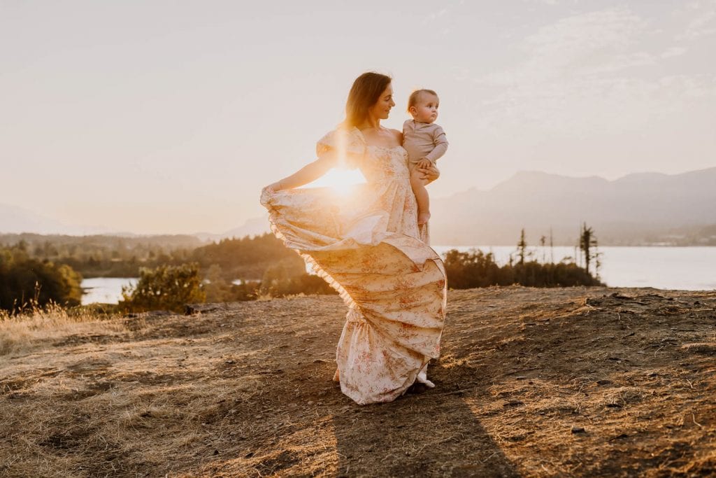 Mom holding her baby boy while swishing her dress at sunset