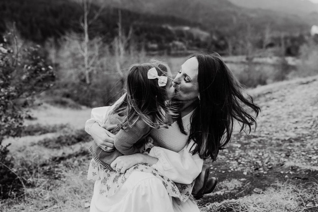 A mom kissing her little girl while the wind blows their hair during photography session