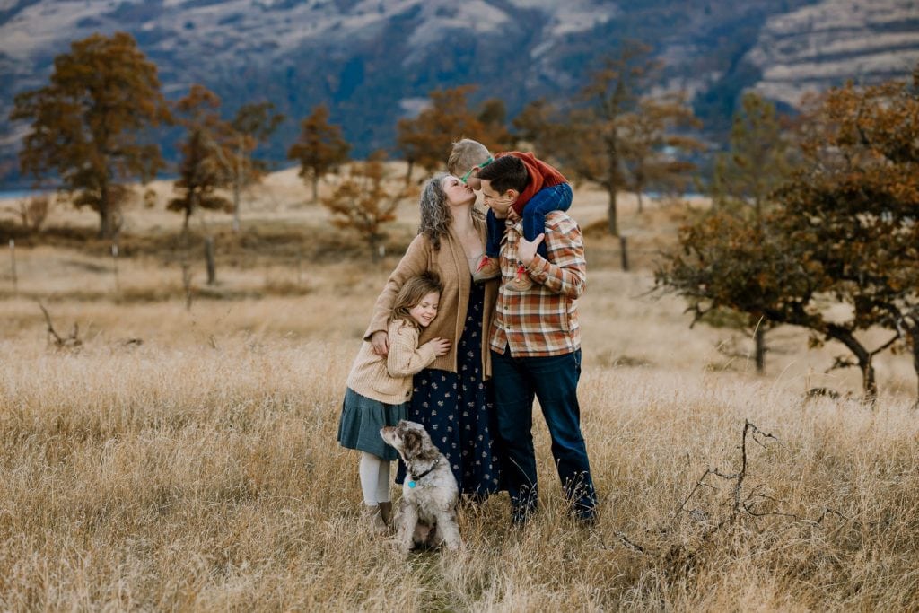 Family hugging in a golden field with mountains behind them