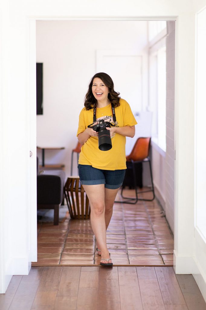 A family photographer holding her camera walking down a hallway and smiling
