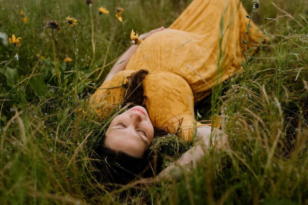 pregnant mom laying in the grass with a lace yellow dress