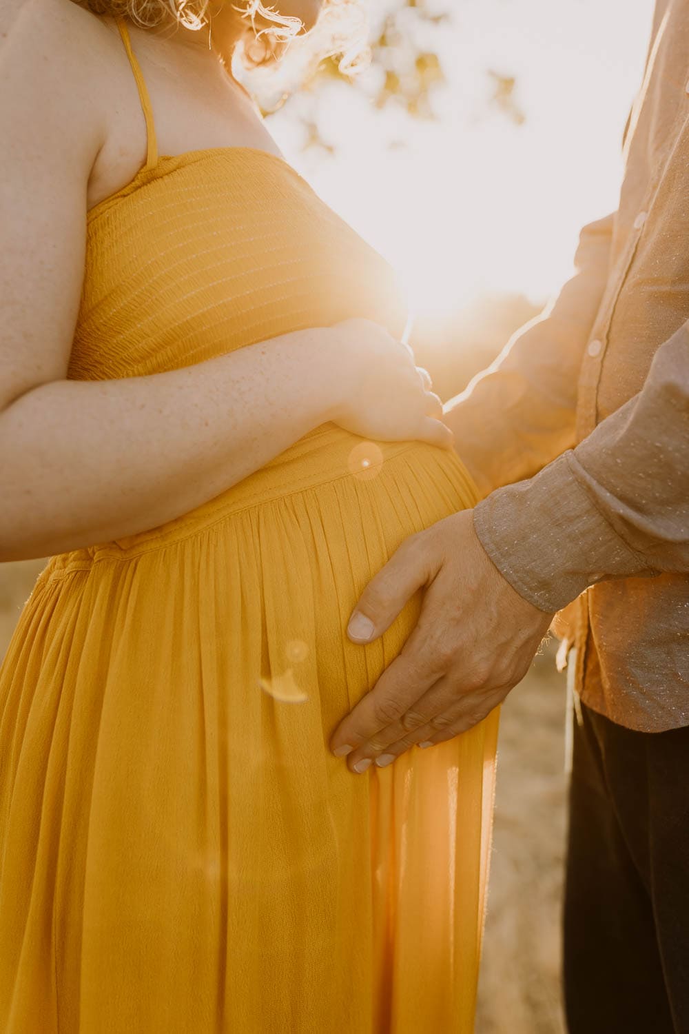 closeup of pregnant mom in yellow dress with husbands hands on belly