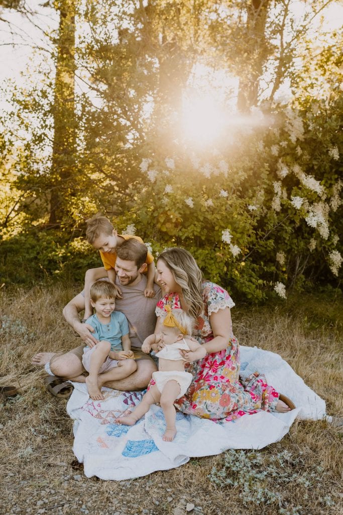 mom, dad, and three kids sitting on a blanket at sunset time during family photos