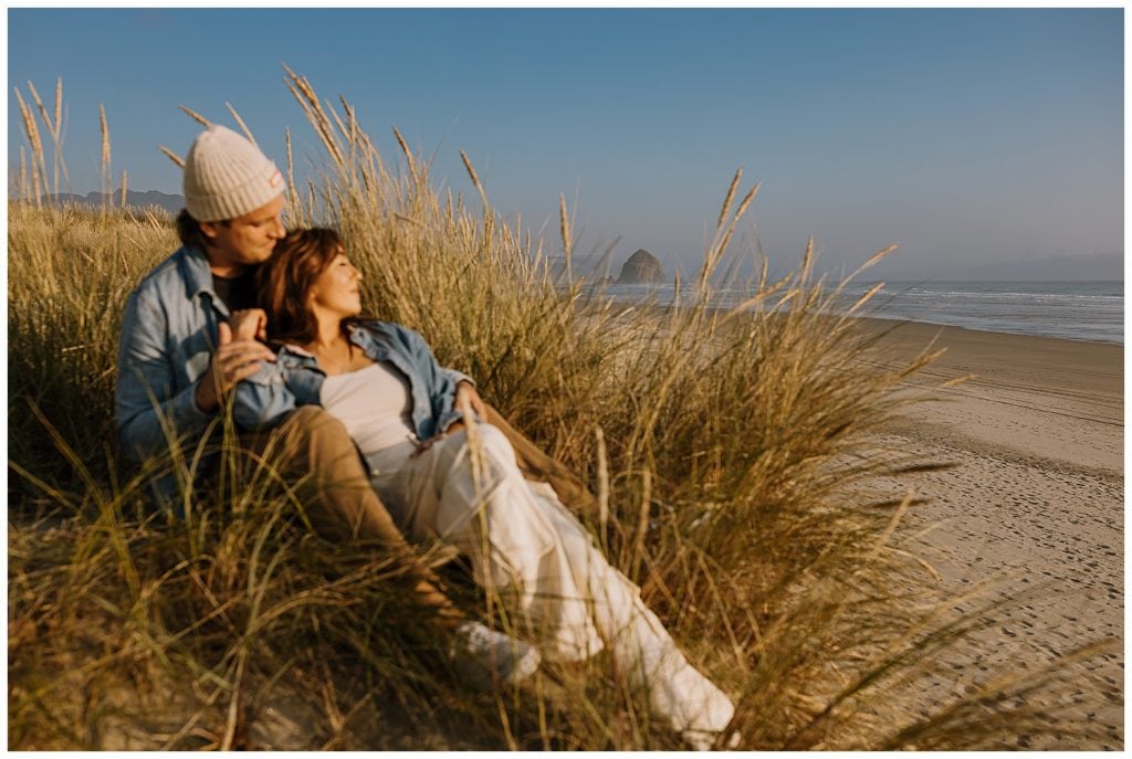 Engaged couple sitting in the beach grass in Cannon Beach