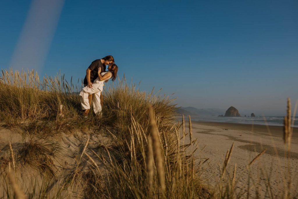Engaged couple embracing on a dune in Cannon Beach