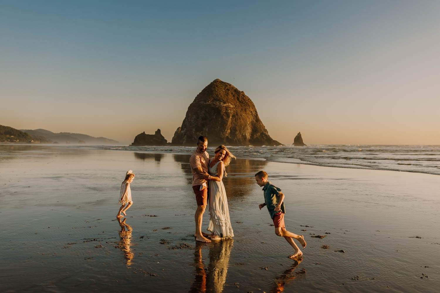 Family running around at the beach with haystack rock behind them