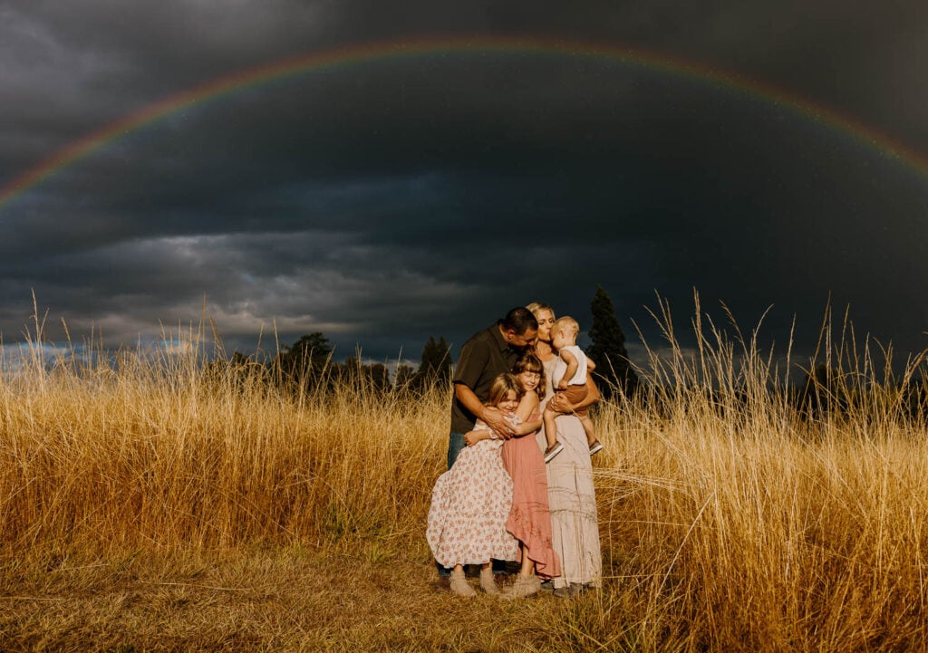 Family hugging under a rainbow in a field