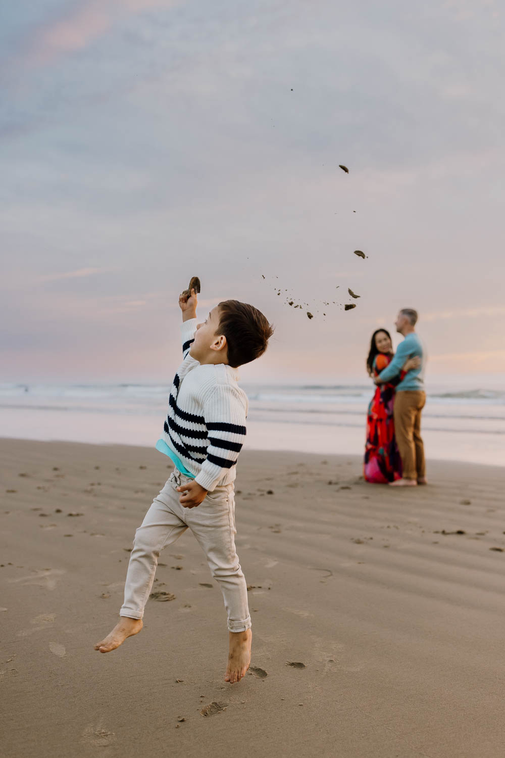 Little boy throwing sand while parents watch