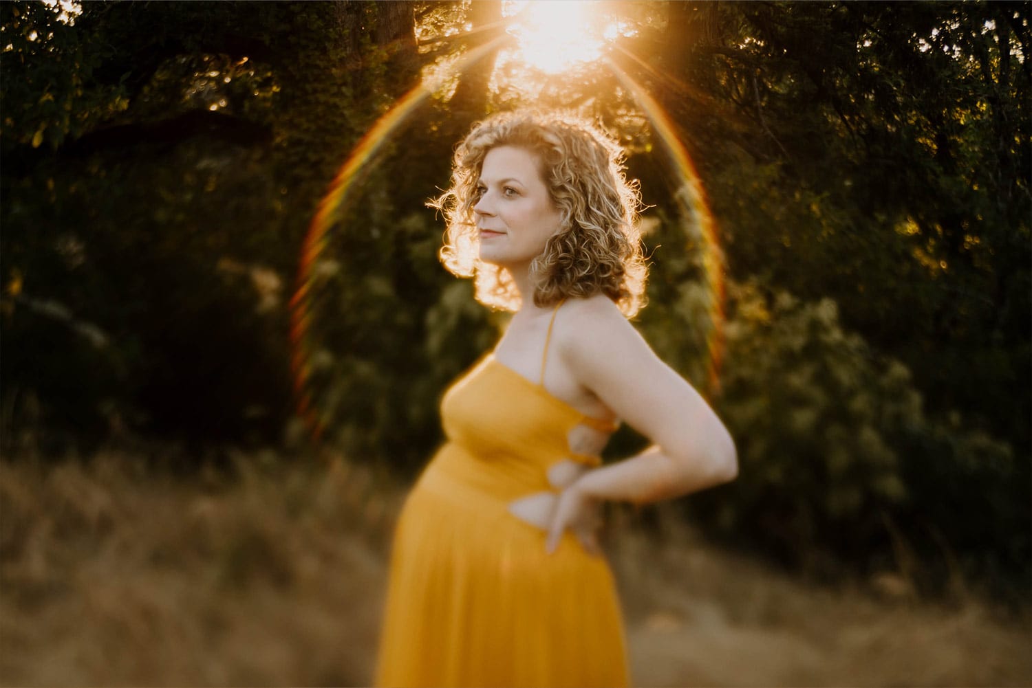 pregnant mom in mustard yellow dress with rainbow over her head