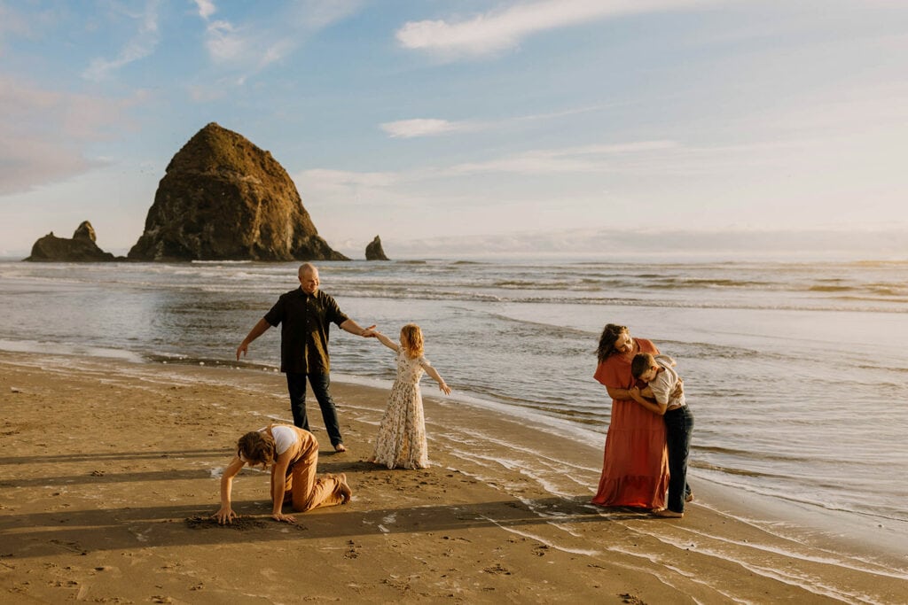 family of five playing at cannon beach and drawing in sand with haystack rock behind them